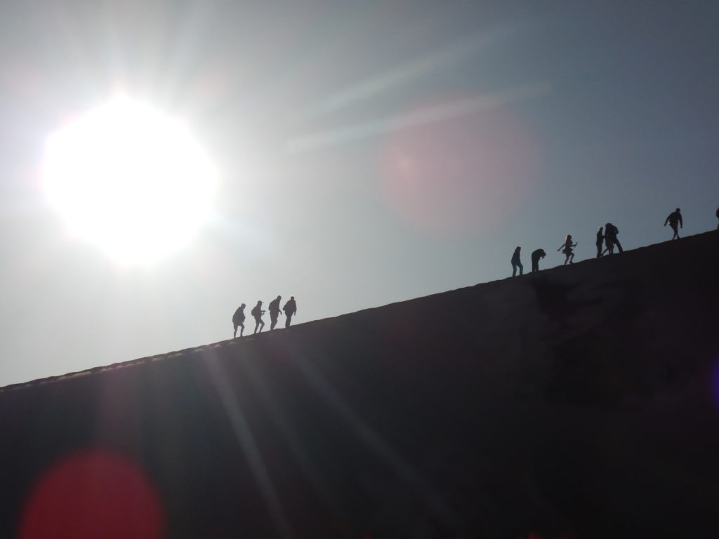 Eight climbers climb Dune 45 in bright sun.