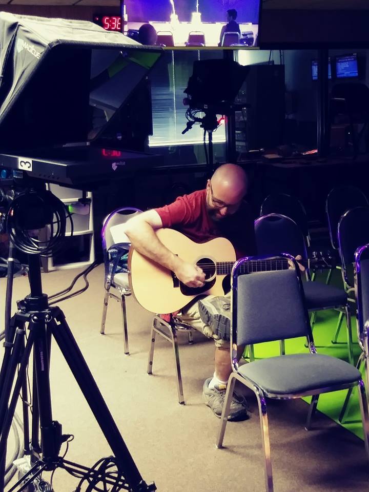 A guitarist strums his guitar in a TV studio.