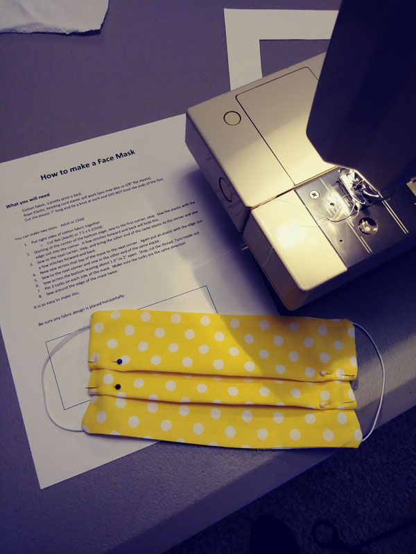 A sewing machine, a set of instructions for making a mask, and a mask with pleats pinned into place.